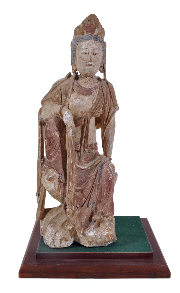 A Chinese wood sculpture of Guanyin sitting on a rocky outcrop with one knee raised, dressed in