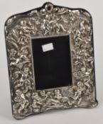 A silver shaped rectangular photoframe, maker`s mark `M & LS`, London 1991, chased with cherubs
