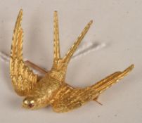 A gold swallow in flight brooch, with realistically engraved decoration, and ruby set eyes, 3.3cm
