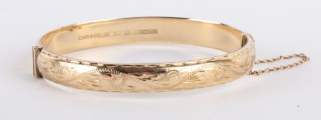 * A 9 carat gold hinged bangle, Birmingham 1992, half engraved, of hollow D section, 8.5mm wide, 5.