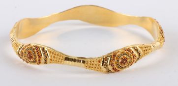 * An Indian bangle, stamped `21K`, of hollow D section, decorated with beading, internal diameter