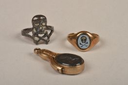 A signet ring, inset with a carved oval hardstone intaglio of a skull and cross bone; a skull and