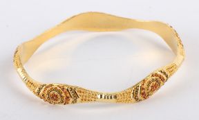 * An Indian bangle, stamped `21K`, of hollow D section, decorated with beading, internal diameter