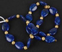 A lapis lazuli bead necklet, the beads of flattened egg shape with gilded textured beads between,