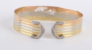 * A diamond set three colour torque bangle, stamped `750`, the flat reeded band, 15mm wide, with C