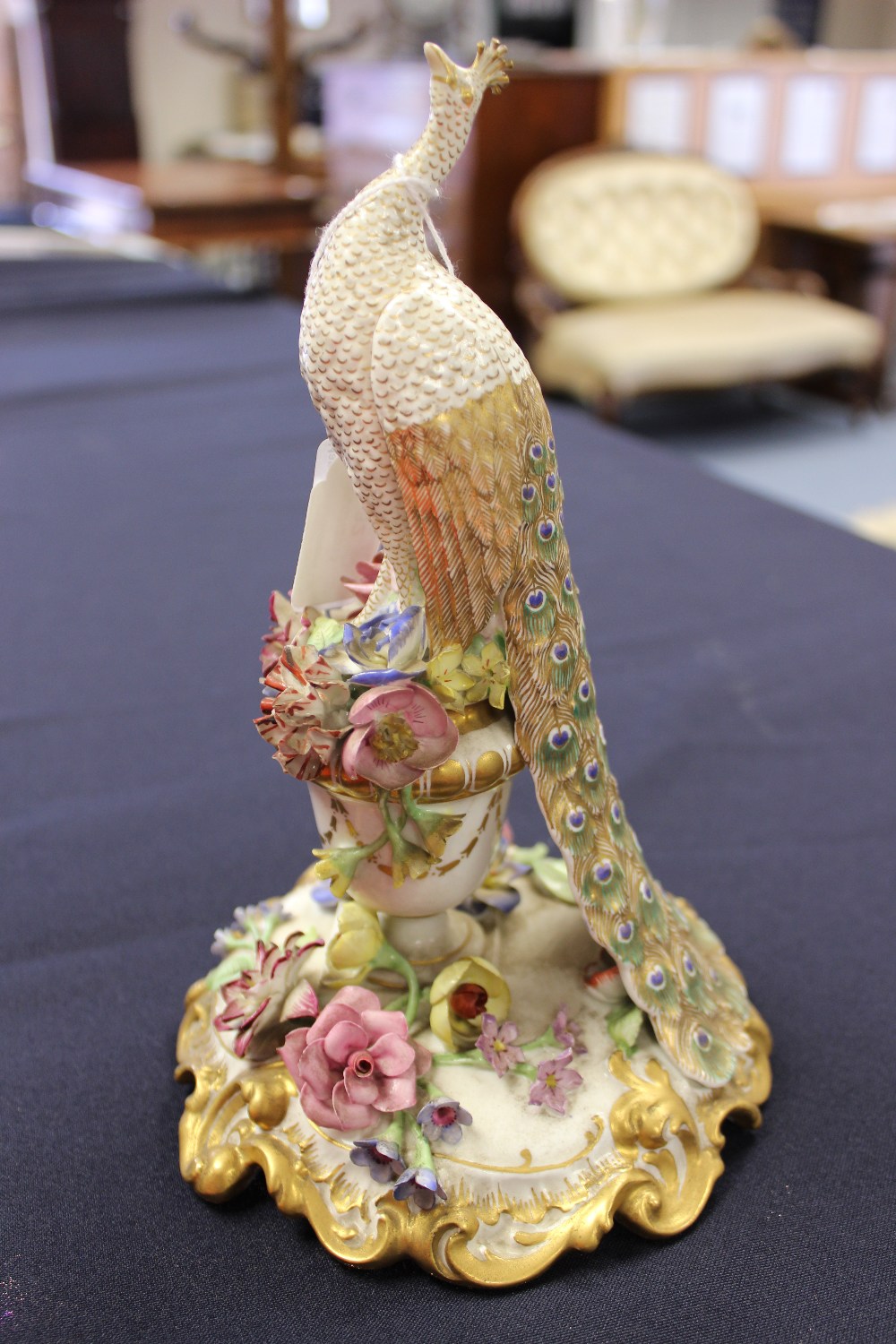 A Royal Crown Derby model of a peacock, standing on a floral encrusted urn, spreading circular