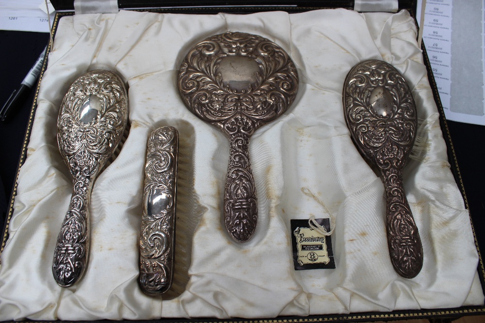 A cased silver backed embossed dressing table set, including a bevelled mirror, with one piece