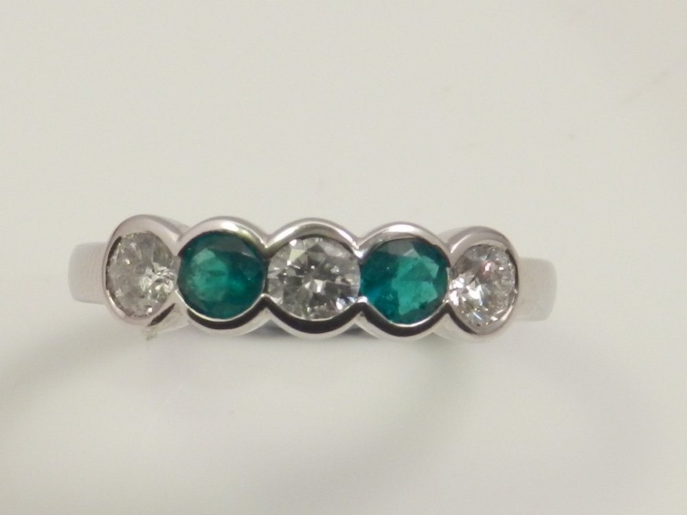 An 18ct white gold five stone emerald and diamond ring, the collette set stone measuring approx.