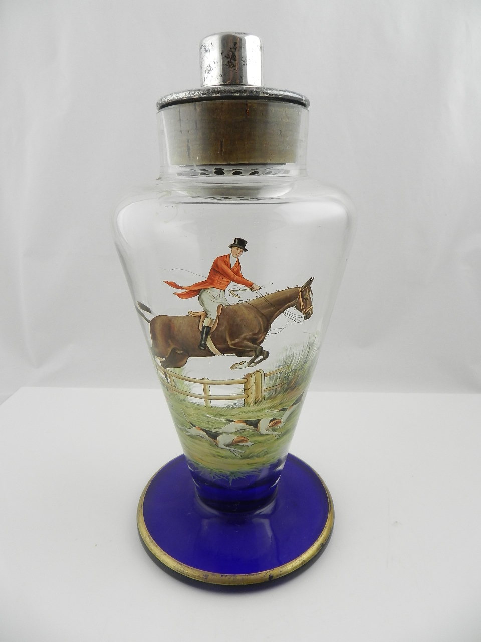 An Art Deco tapering glass cocktail shaker painted with a hunting scene on blue and gilt spreading