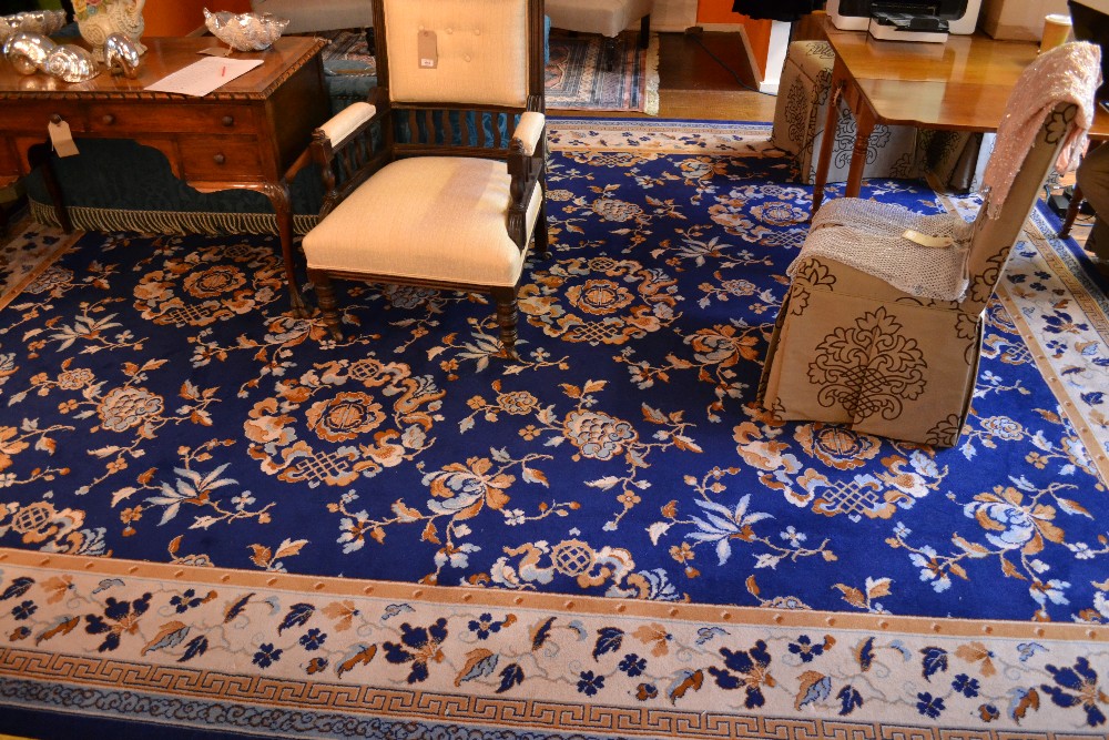 A large rug decorated with floral designs on a blue ground contained by borders. 350x456cm.