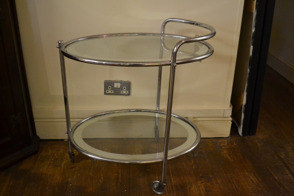 A chrome and glass two tier serving trolley of oval form raised on castors.