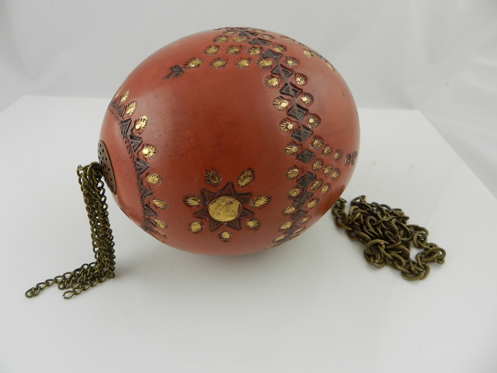 A Turkish terracotta tophane egg having gilt encised decoration hanging from a suspensory chair