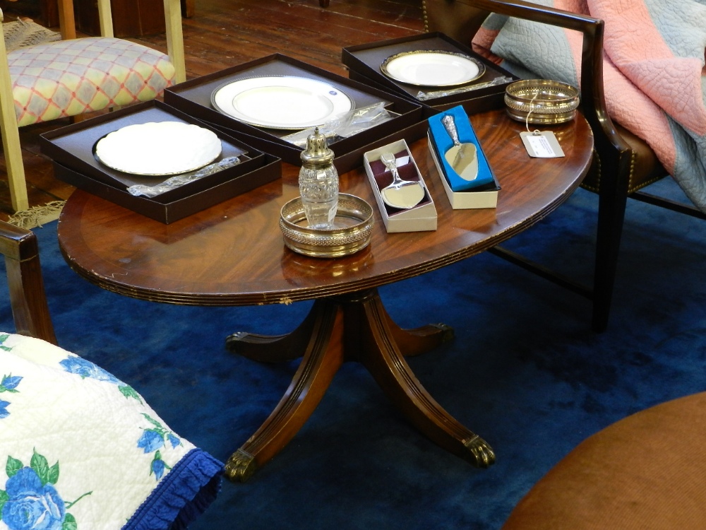 An inlaid crossbanded pedestal low table of oval form raised on quadraform out swept supports.