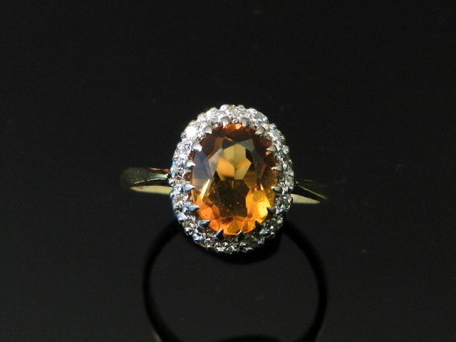 An 18ct yellow gold ring having an oval Imperial golden topaz surrounded by diamonds.