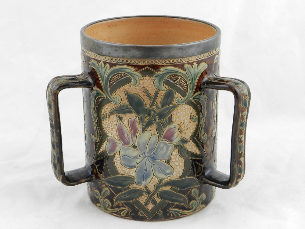 A Doulton Lambeth three handled loving jug, the sides decorated with panels of flowers and leaves