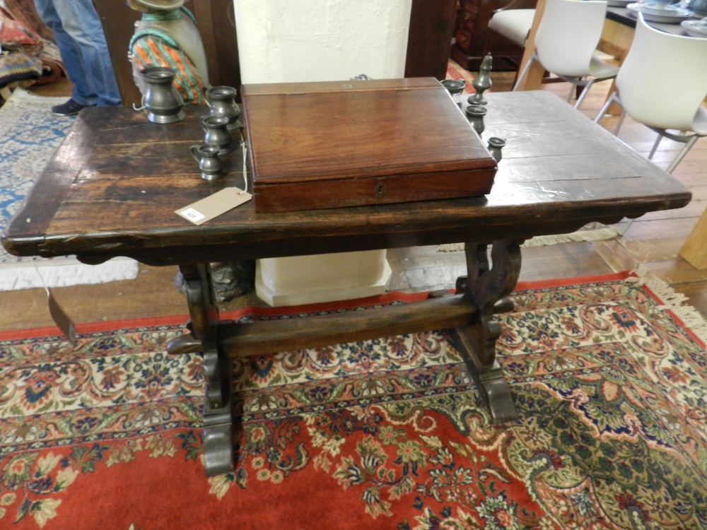 An oak plank topped table raised on pierced stile end support joined by stretchers