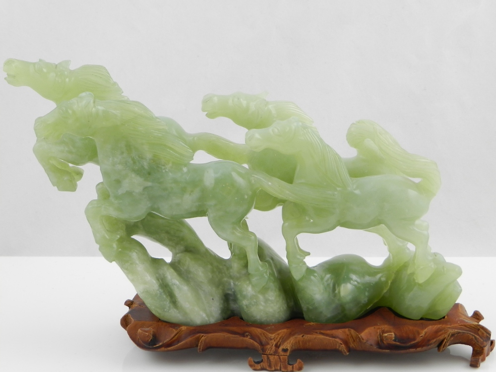 A Chinese carved green jade carving on a wooden stand depicting four leaping horses.