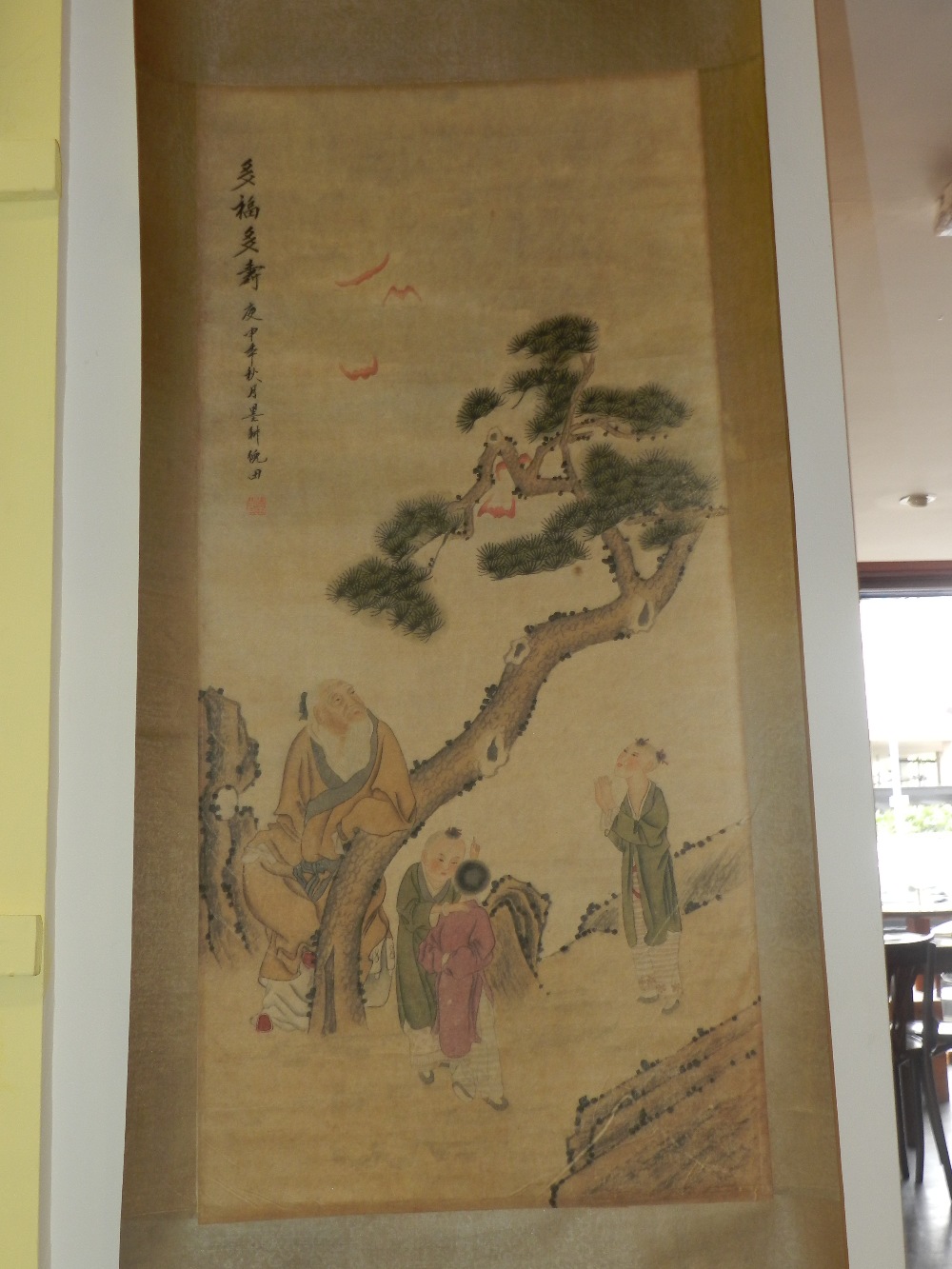 A Chinese scroll picture depicting various figures under a fruit tree with bats.