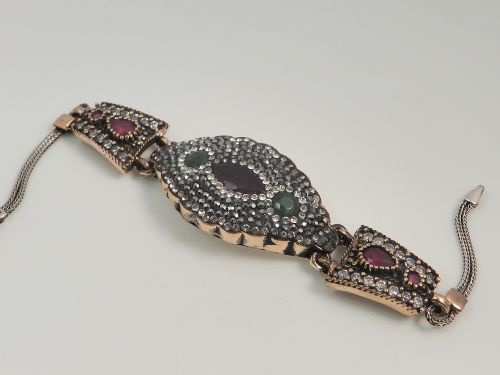 A white metal backed bracelet set with faux rubies, emeralds and diamonds.