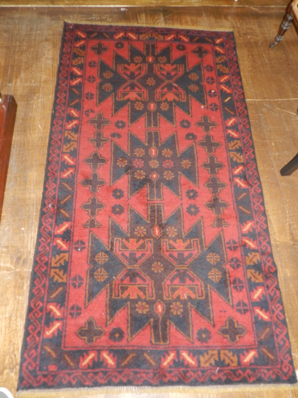 A Baluch rug having geometric medallion on a red ground contained by borders. 200 x 107cm.