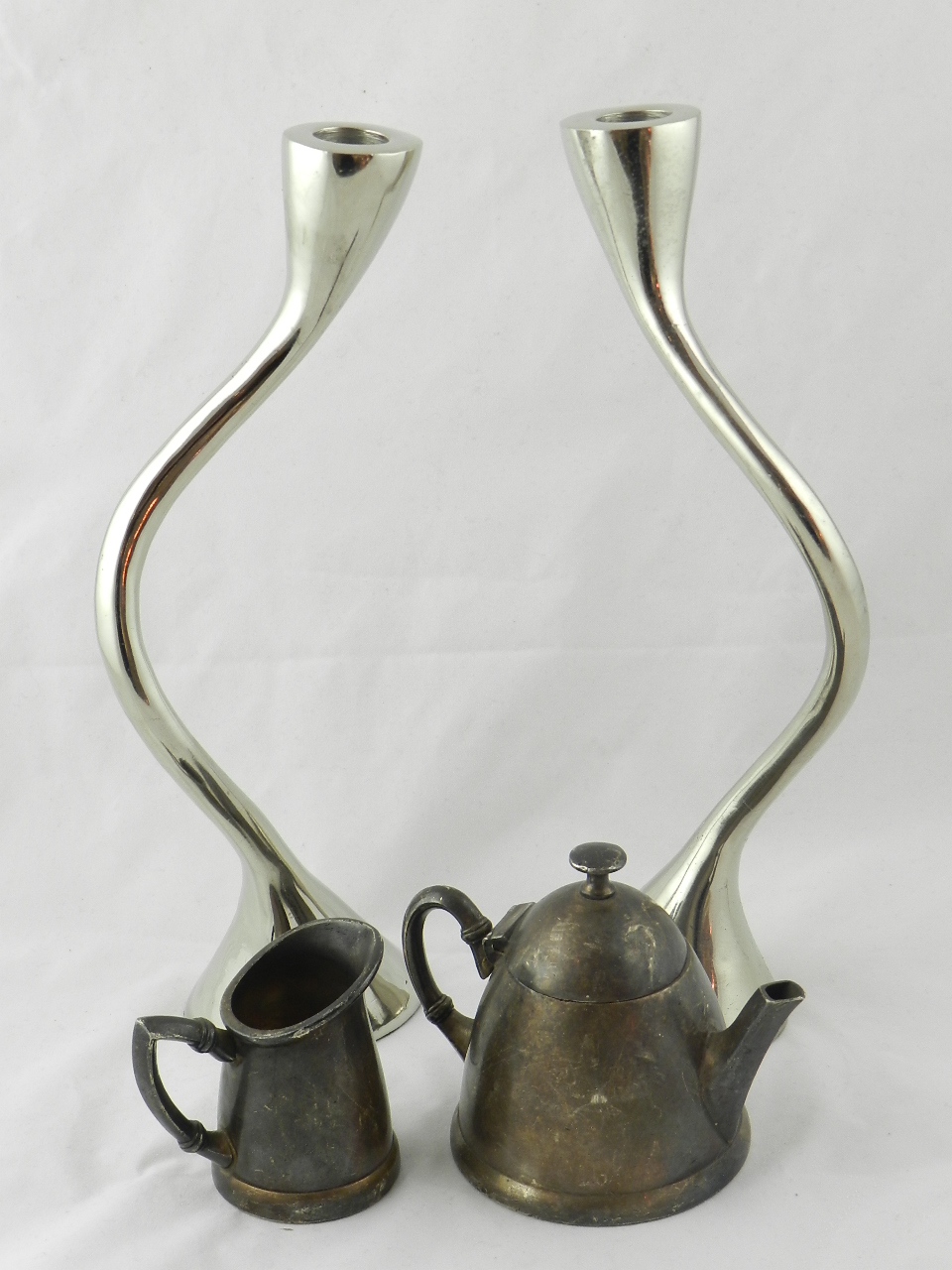 A pair of chrome candlesticks of innovative curved form and a plated teapot and milk jug with ZS