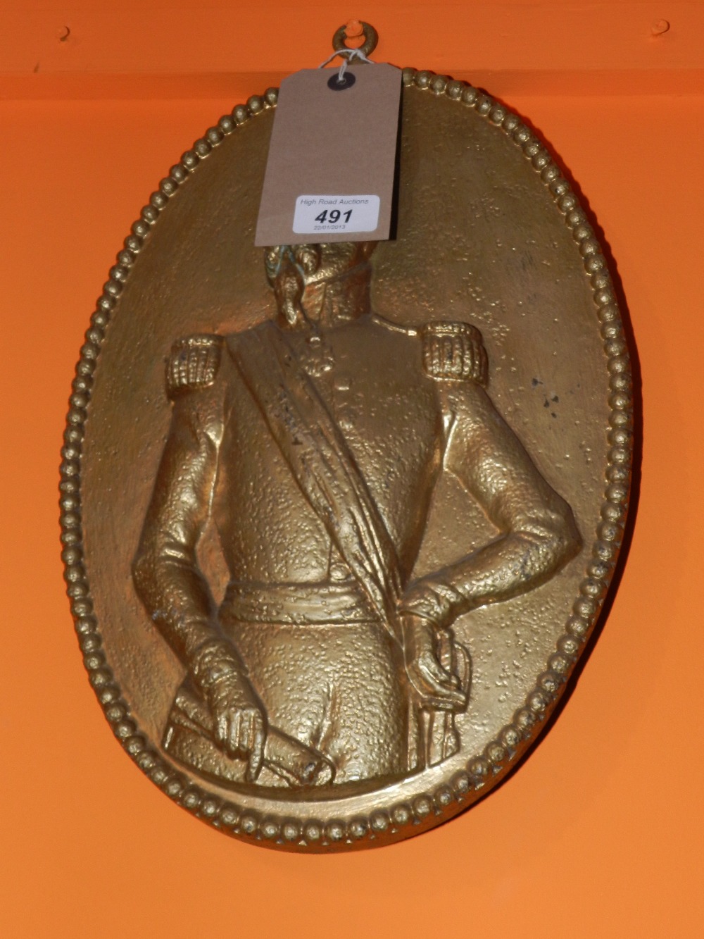 A gilt painted cast iron wall plaque of oval form depicting an officer.