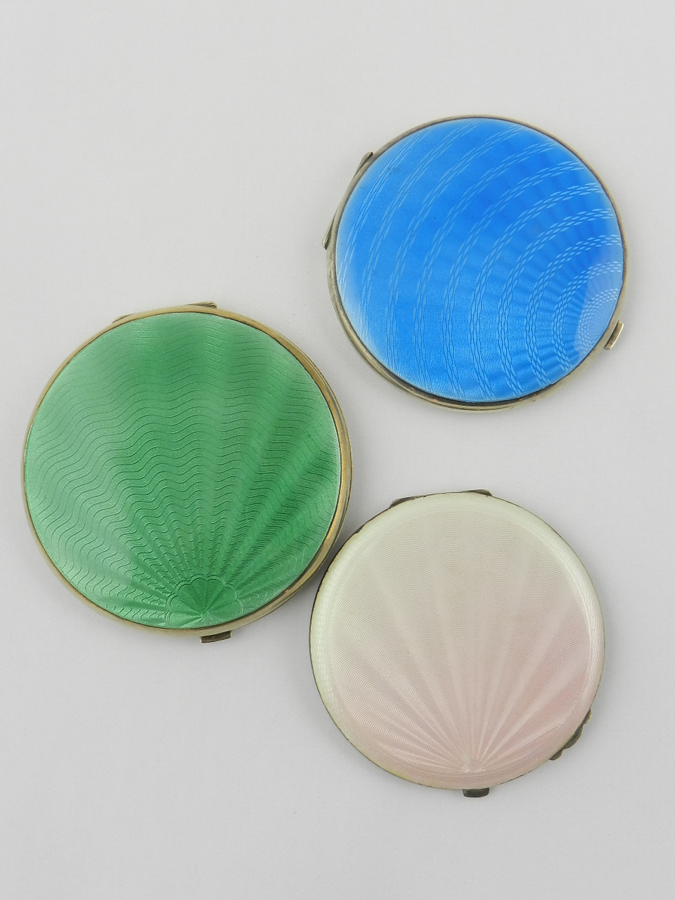 Three guilloche enamel compacts of circular form with bar push clasps.