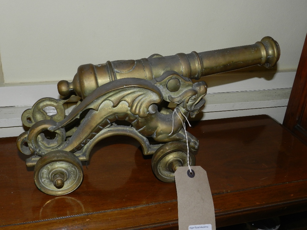 A vintage brass cannon supported by winged dragons on a rolling base.