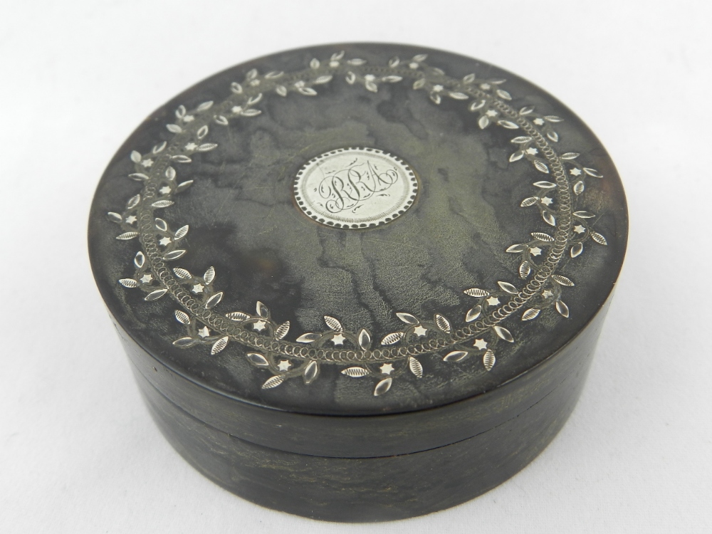 A 19th century tortoiseshell circular snuff box with silver leaf decoration and central silver