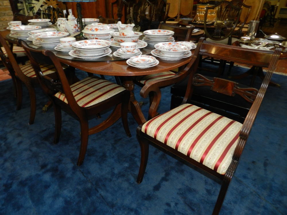 An oval Regency mahogany dining table with four matching chairs and two carvers, upholstered in