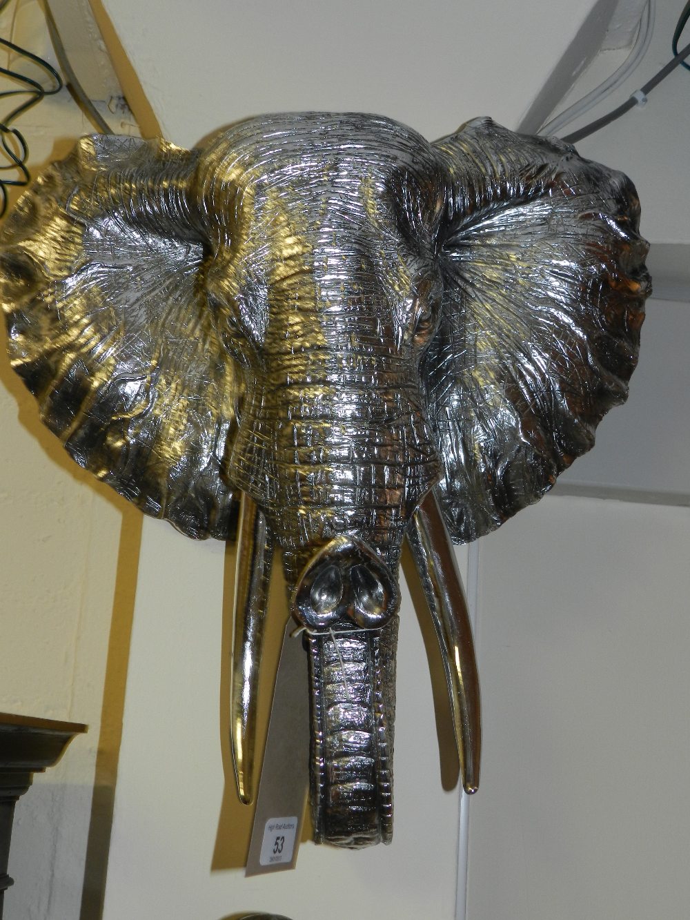 A silvered wall hanging in the form of an elephants head.