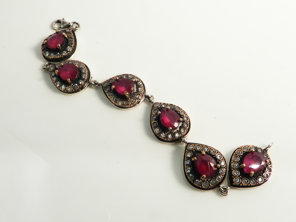 A sterling silver bracelet having heart shaped links studded with faux diamonds and rubies.