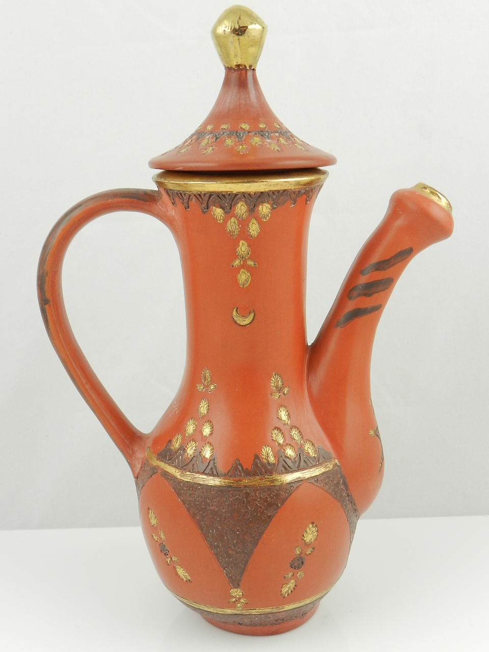 A Turkish red terracotta coffee pot incised with gilt highlighted geometric shapes and with domed