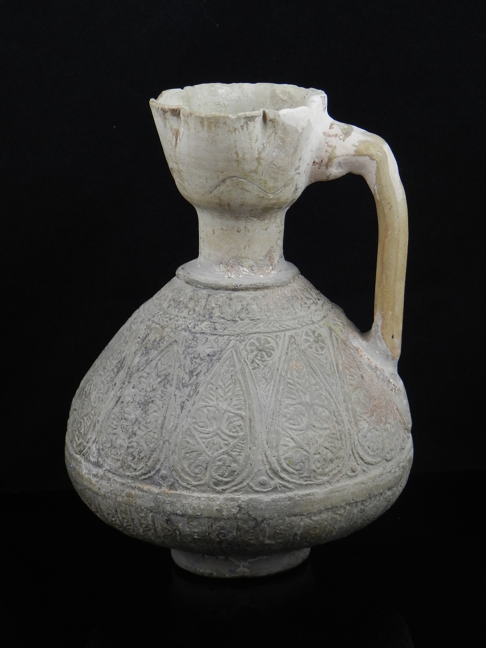 An Islamic earthenware oil jug of compressed pear shape with angled handle; the sides incised with