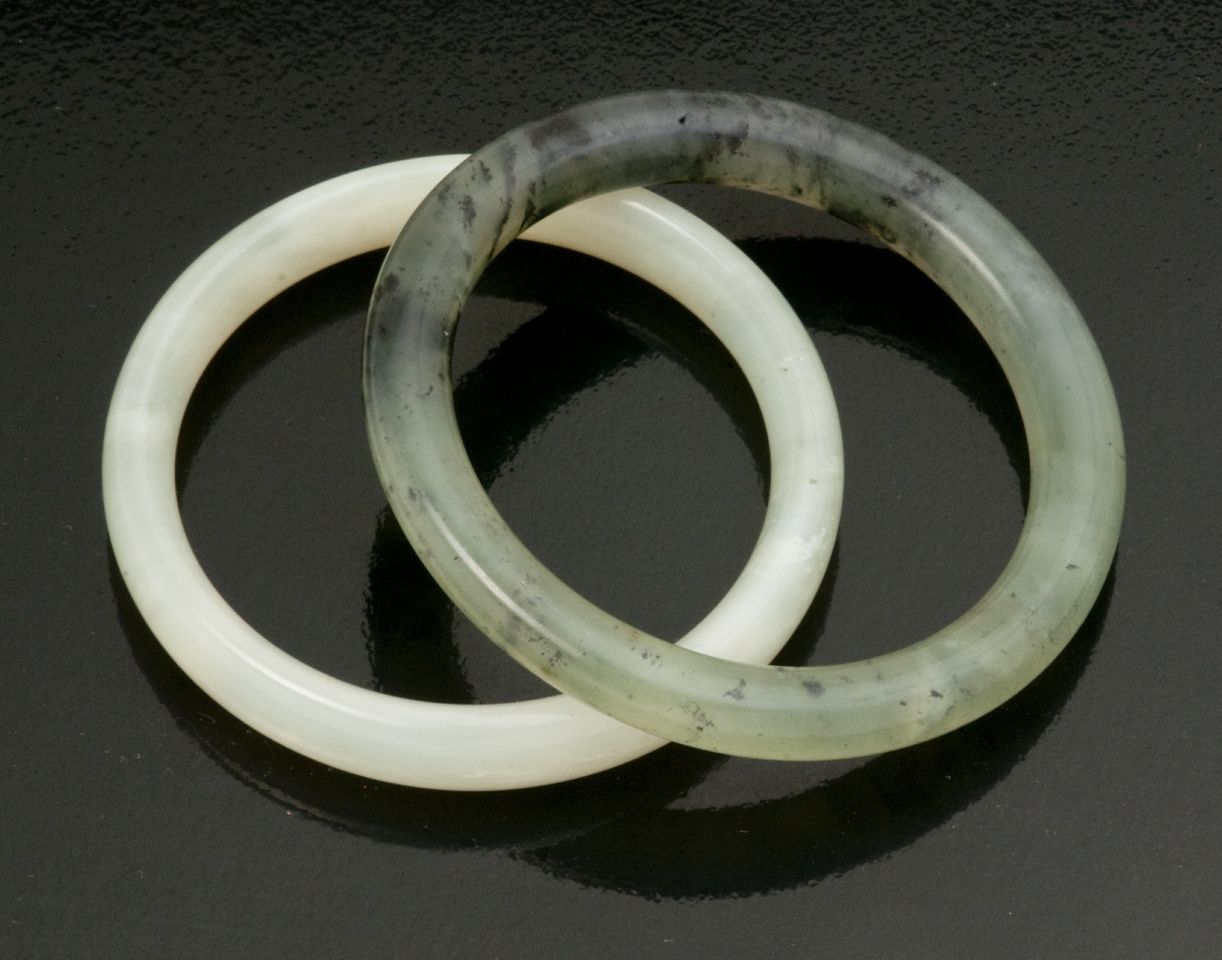 A celadon jade bangle of oval cross section; together with a spinach green jade bangle of circular