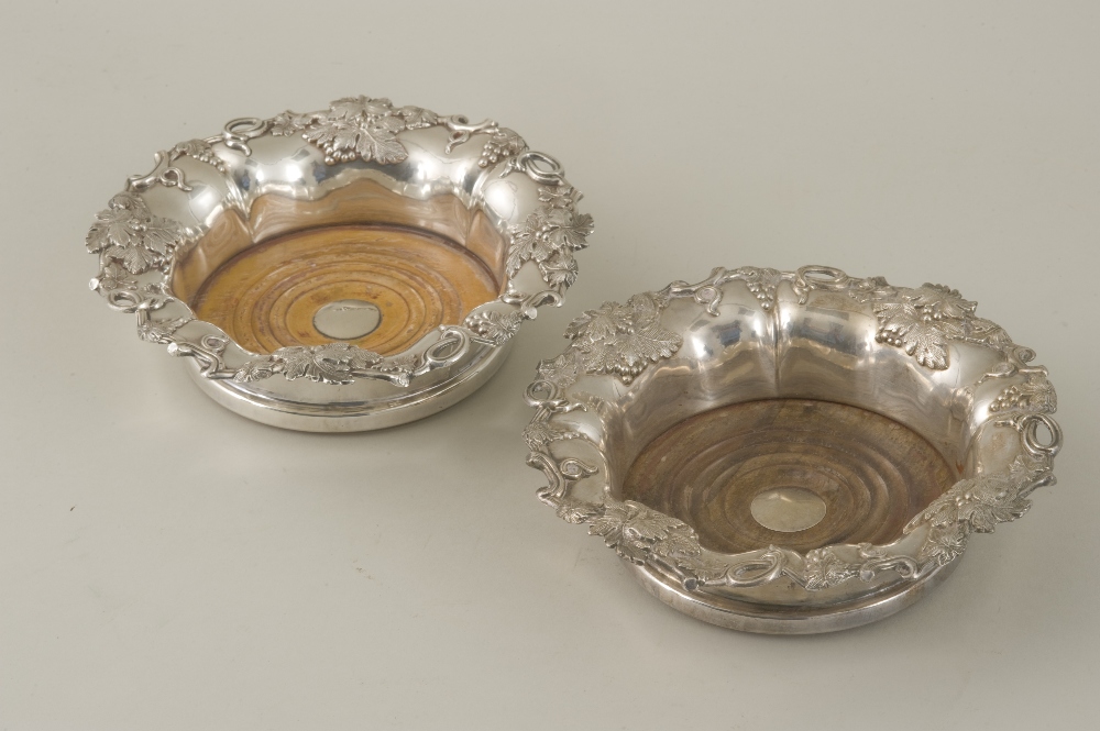 A pair of silver plated wine coasters, the everted rim decorated with grape and vine decoration over