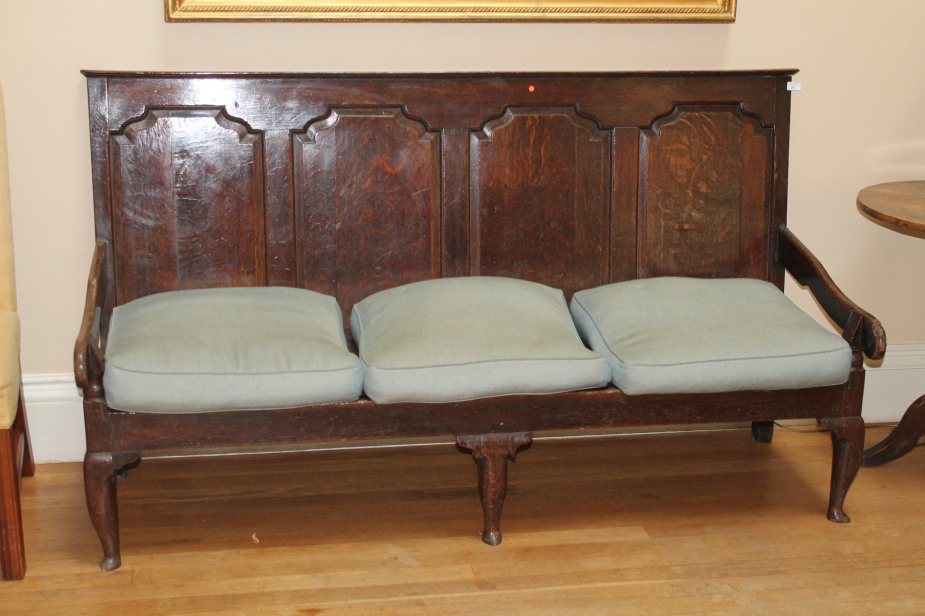 An early 18thC oak settle, with four fielded panels to the back, slatted seat with loose squabs