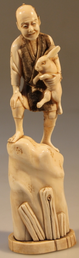 An early 20thC Japanese carved okimono of a peasant holding a rabbit on a rock, 21cm high. (AF)