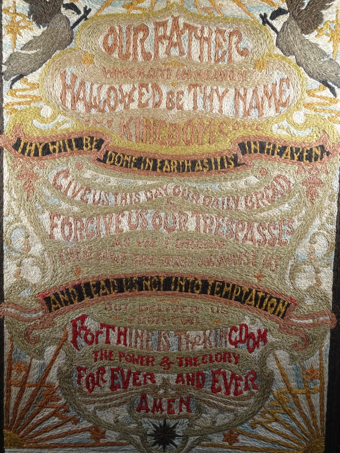 A Victorian silk work panel, embroidered with the Lords Prayer against a celestial ground, 70cm x