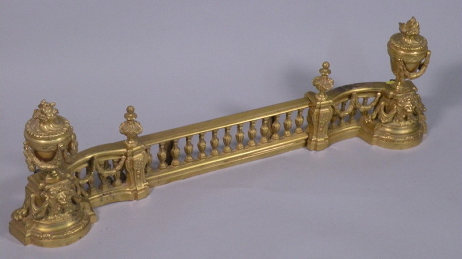 A French gilt metal fender, cast with lion heads, urns and flames, 100cm wide.