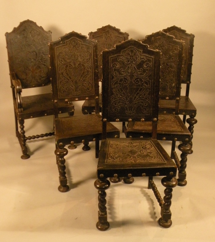 A set of six ebonised continental dining chairs, each with an embossed leather and brass studded