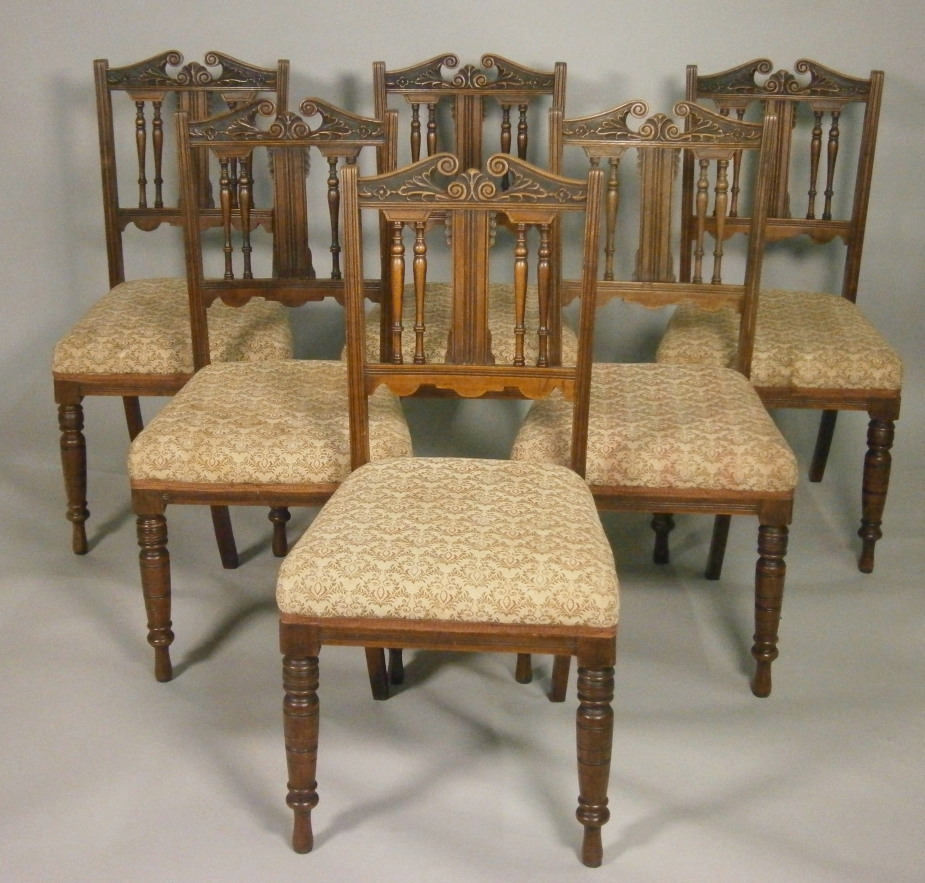 A set of six Edwardian walnut dining chairs, each with a carved rail back and a padded seat, on