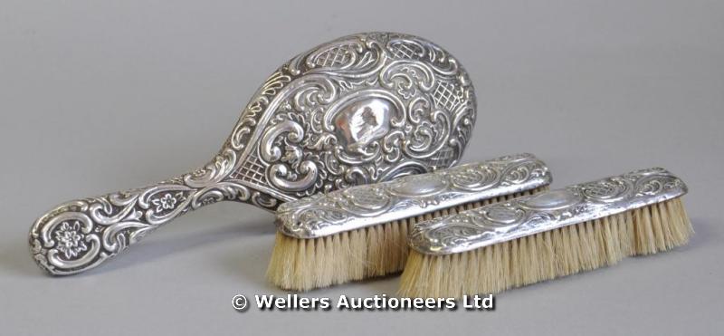 "A silver hand mirror, with scroll and flower decoration; and a pair of clothes brushes,