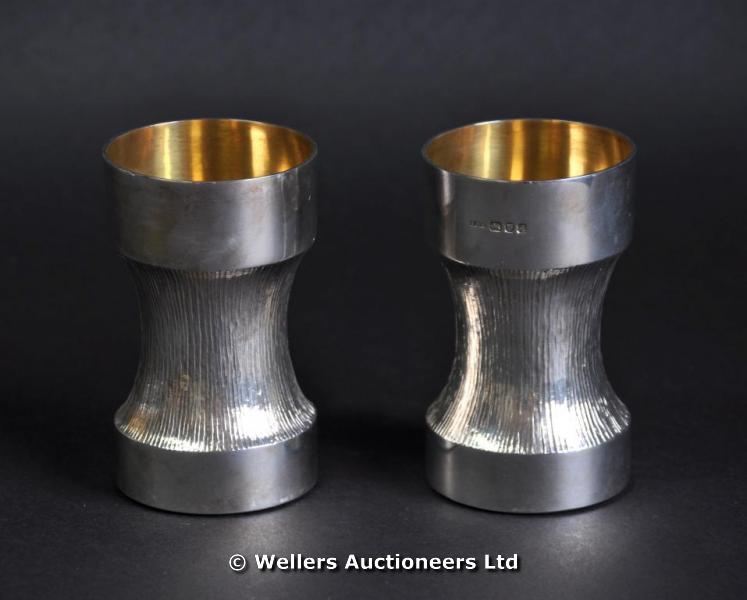 "A pair of silver waisted beakers, the central section with bark design, gilded interior, London