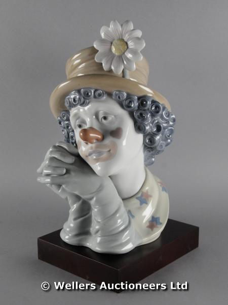 "A Lladro portrait bust of a clown wearing a hat, his hands clasped, with a separate wooden stand,