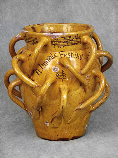A LARGE EWENNY POTTERY WASSAIL, having nineteen loop handles, decorated in mottled yellow glaze.