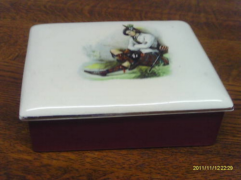 A porcelain trinket box and cover, early 20th Century, decorated with a Scottish man resting, a