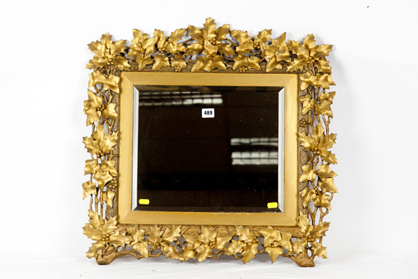A bevelled wall mirror in a gilt wood holly and ivy leaf frame, overall size 23 ins (58 cms) x 25