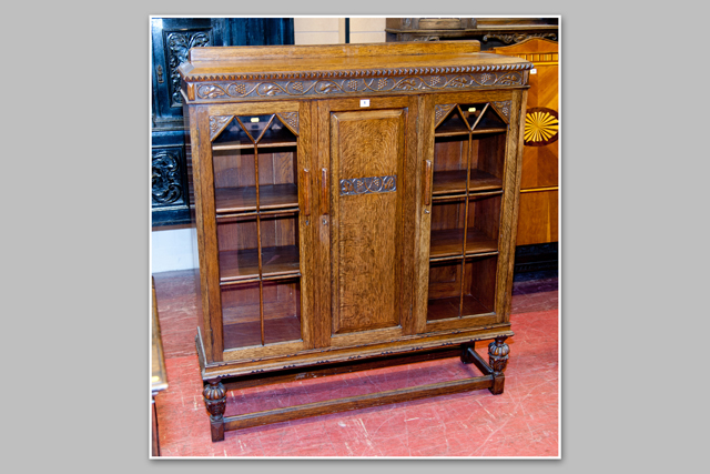 A 1930s polished standing bookcase having a centre panel door with glazed door either side to an