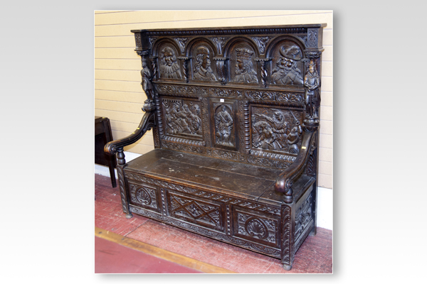 A late 19th Century carved oak settle, the back having four inset figure panels with three panels